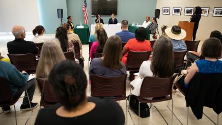 Photo from behind attendees of the event, showing the panelists. 