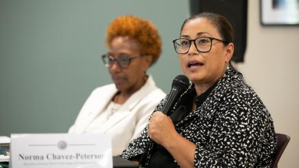 Image of Norma Chavez-Peterson speaking at microphone. Vernita Guiterrez is in the background.